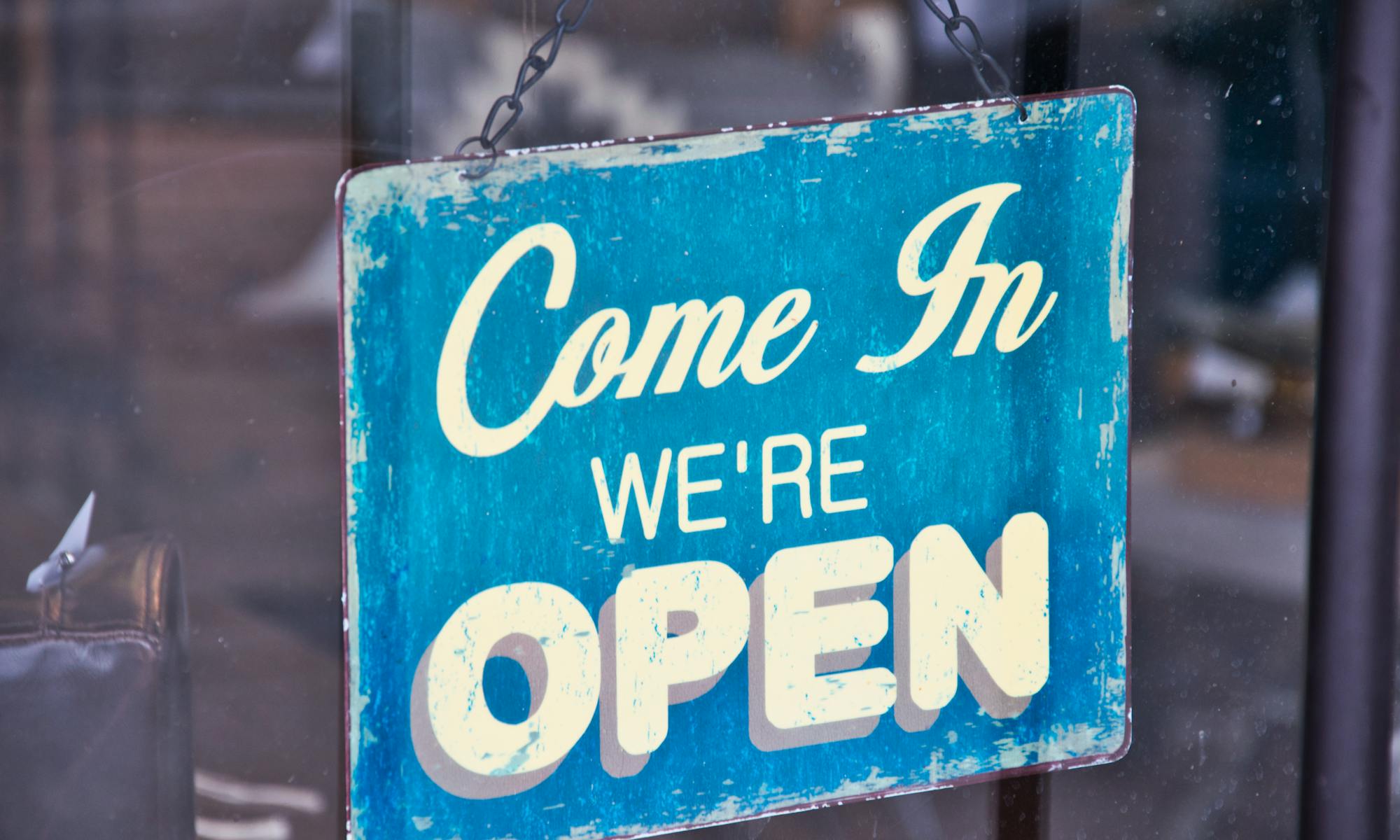 Retro blue open sign on a shop glass door inviting customers in.